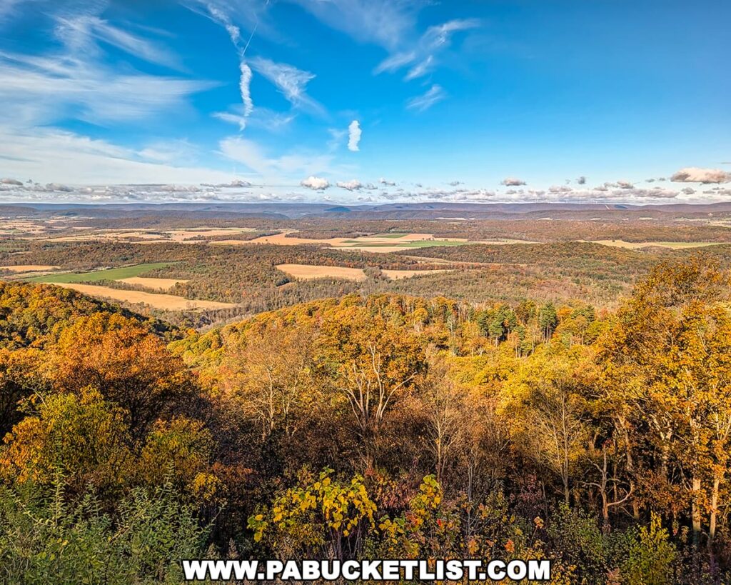 Panoramic view from Colerain Road Vista in Rothrock State Forest, featuring rolling ridges, patchwork farm fields, and vibrant October foliage beneath a bright blue sky streaked with wispy clouds.