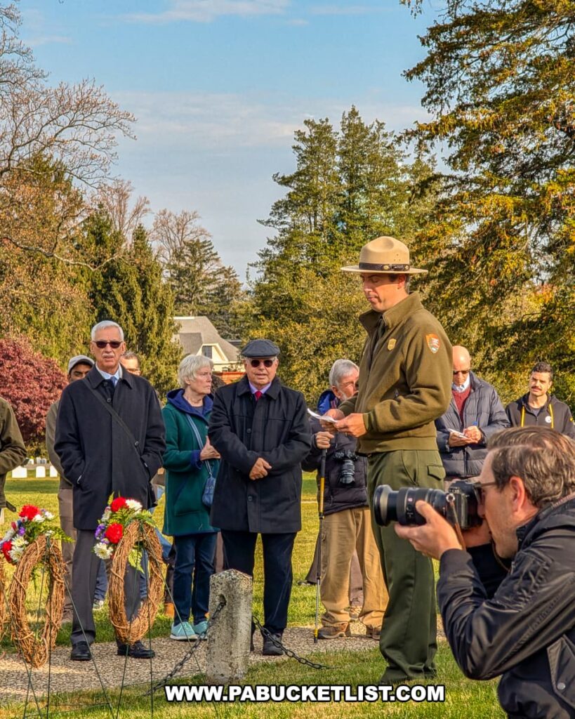A National Park Service ranger speaks beside wreaths during the Dedication Day ceremony at Soldiers’ National Cemetery in Gettysburg as attendees and photographers look on respectfully.