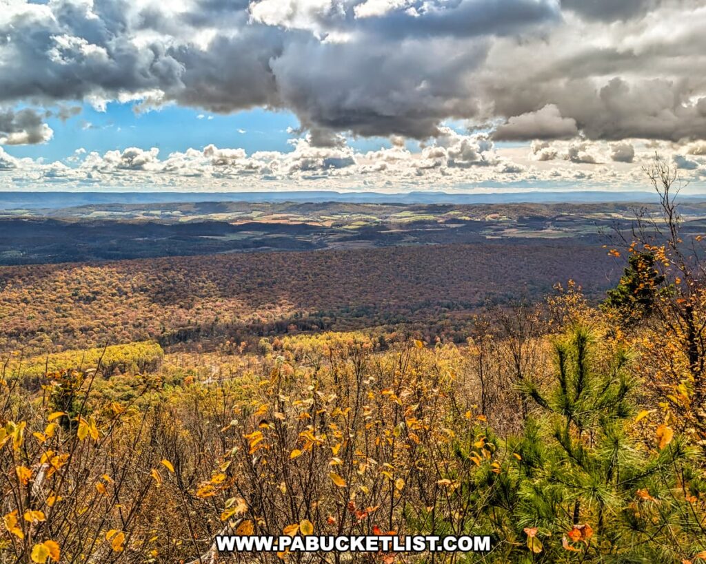 Expansive autumn view from Fire Tower Vista along the Mid State Trail in Rothrock State Forest, overlooking layers of forested ridges, rolling farmland, and distant mountains beneath a dramatic sky filled with sunlit clouds.