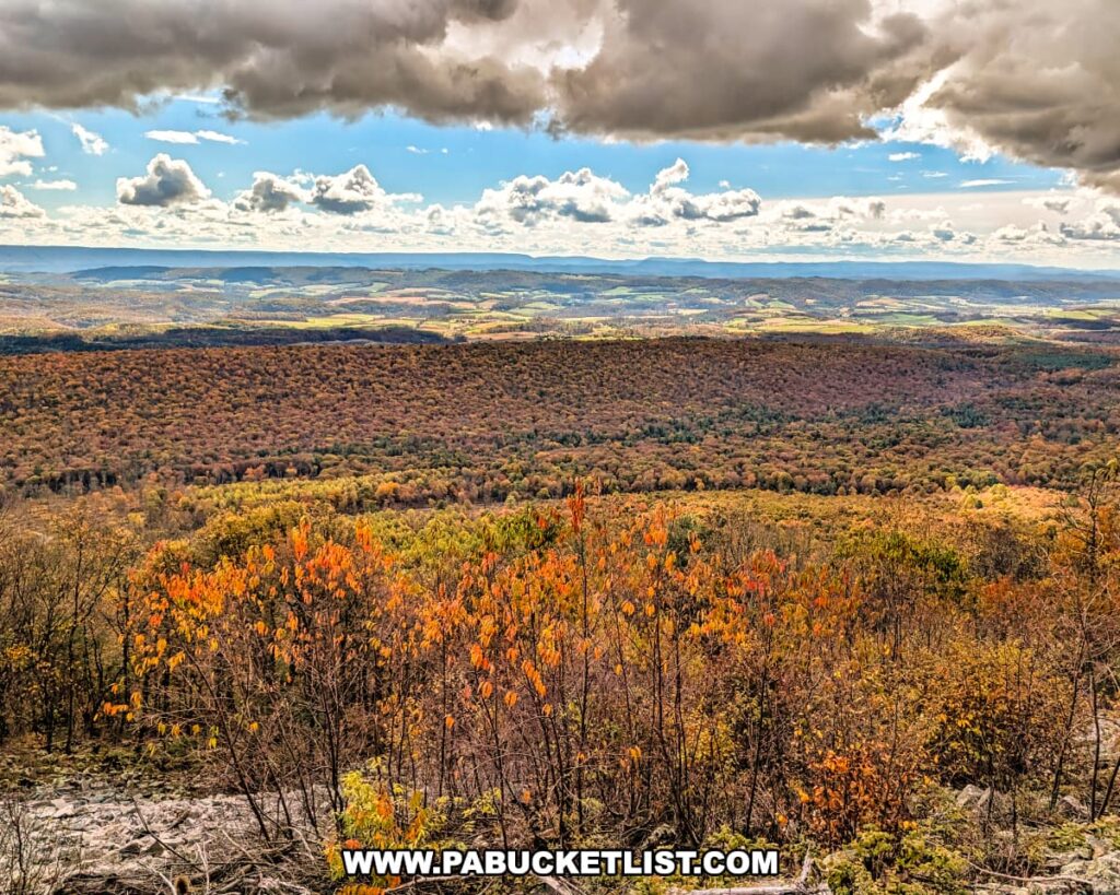 Sweeping autumn view to the south from Harry’s Valley Vista in Rothrock State Forest, showcasing colorful ridges, distant farmland, and layers of mountains beneath dramatic clouds and patches of blue sky.