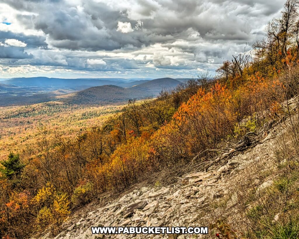 Scenic autumn view to the southwest from Harry’s Valley Vista in Rothrock State Forest, highlighting rocky slopes, vibrant fall foliage, and layers of forested ridges extending toward the distant mountains under a dramatic sky.