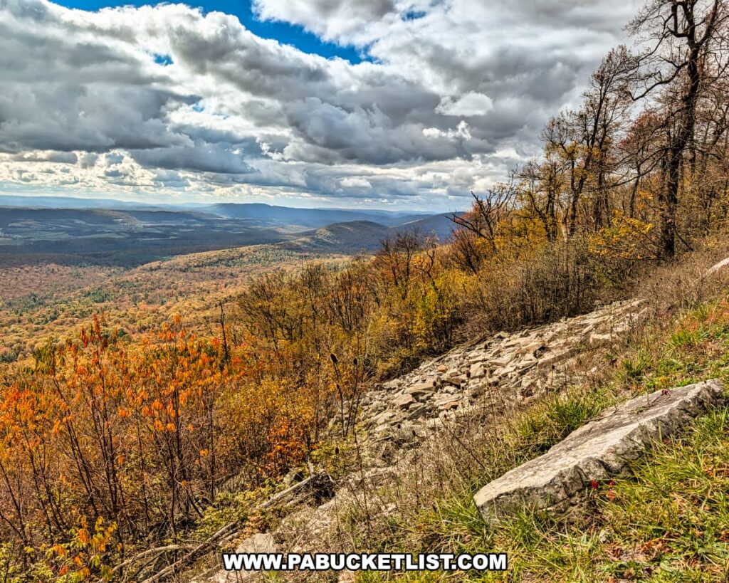 Breathtaking autumn view to the west from Harry’s Valley Vista in Rothrock State Forest, featuring rocky outcrops, colorful foliage, and rolling ridges fading into the distance beneath a mix of bright sunlight and dramatic clouds.