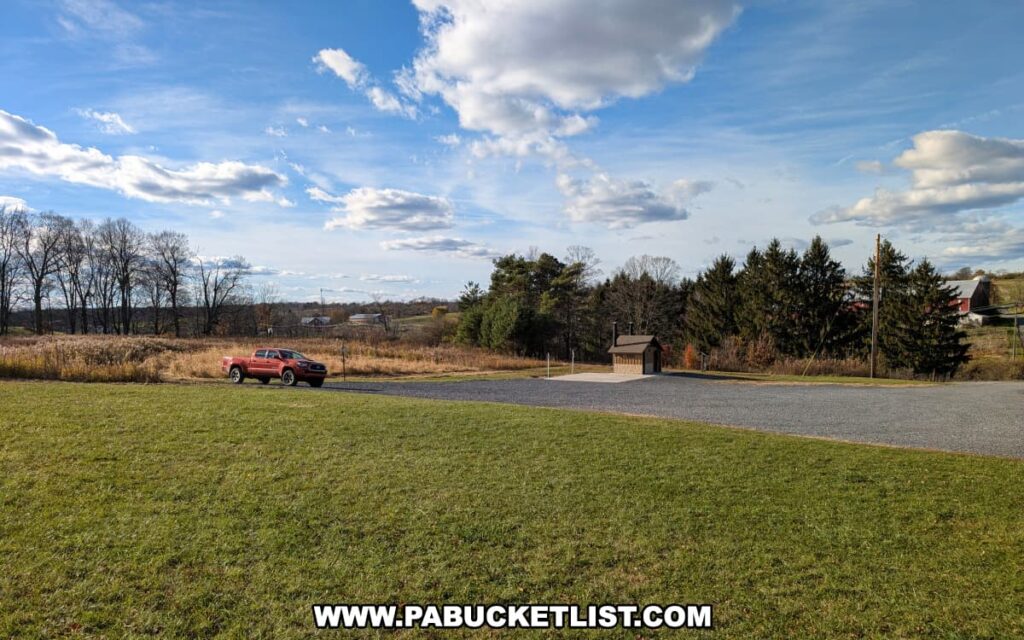 Gravel parking area near the Musser Gap Trailhead in Rothrock State Forest with a red pickup truck, restroom facility, open fields, and farm buildings in the distance under a bright blue sky with scattered clouds.