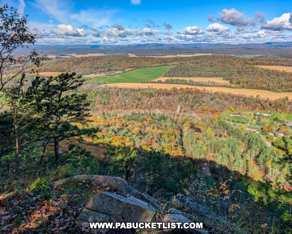 Sweeping October view from Indian Lookout in Rothrock State Forest, with layered ridges, colorful woodlands, open farm fields, and rural homes stretching out beneath a bright blue sky dotted with puffy clouds.