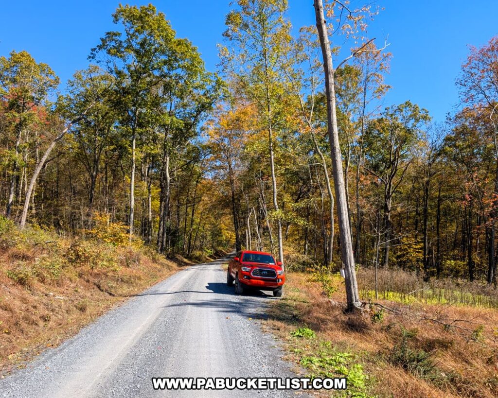 Red pickup truck parked along Harry’s Valley Road near the Indian Steps Trail in Rothrock State Forest, surrounded by tall trees with colorful autumn foliage under a clear blue sky.