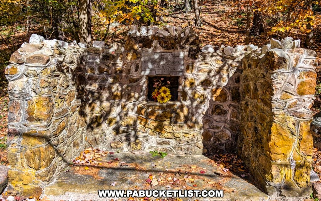 The Chestnut Spring Monument at Mont Alto State Park in Franklin County, Pennsylvania, a stone structure built into a hillside with a plaque and a small alcove holding bright yellow flowers, surrounded by autumn leaves and forest scenery.