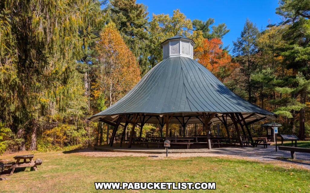 The historic dance pavilion at Mont Alto State Park in Franklin County, Pennsylvania, surrounded by colorful autumn foliage and tall evergreens under a clear blue sky.