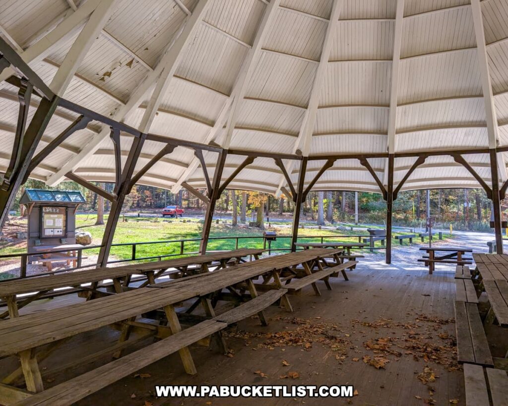 The interior of the historic dance pavilion at Mont Alto State Park in Franklin County, Pennsylvania, featuring wooden picnic tables beneath a high, white, circular roof supported by dark wooden beams, with views of the surrounding forest and park grounds.