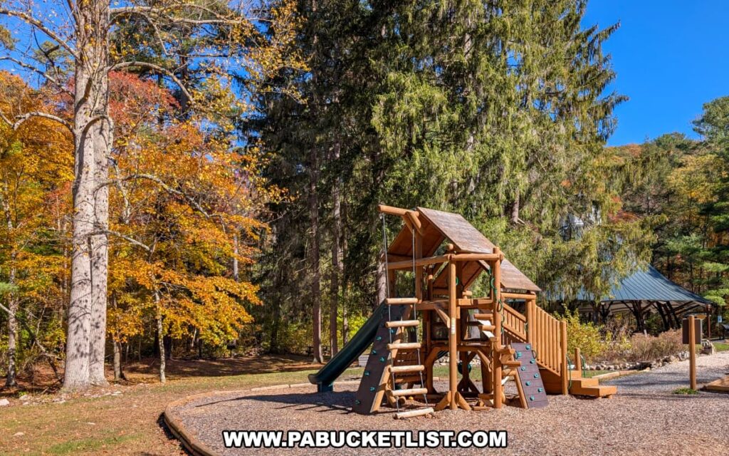 A wooden playground structure with slides and climbing features at Mont Alto State Park in Franklin County, Pennsylvania, surrounded by tall evergreens and colorful autumn foliage under a bright blue sky.