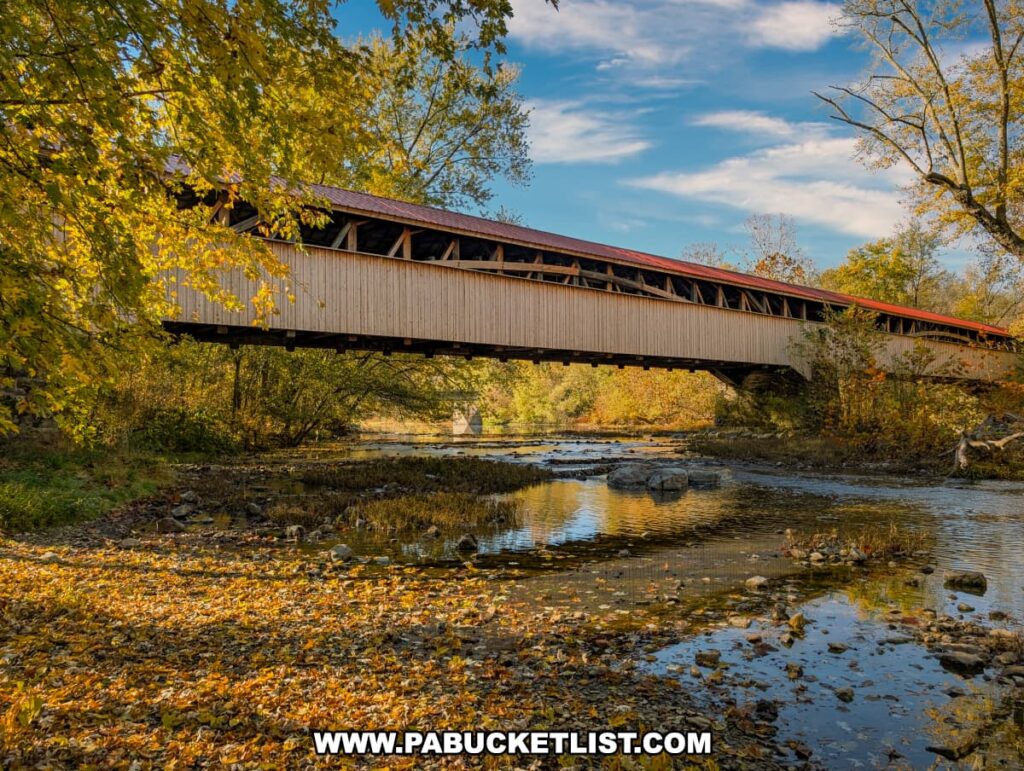 Wide downstream view of the Pomeroy-Academia Covered Bridge in Juniata County, surrounded by golden October foliage and reflected in the shallow, leaf-lined waters of Tuscarora Creek.