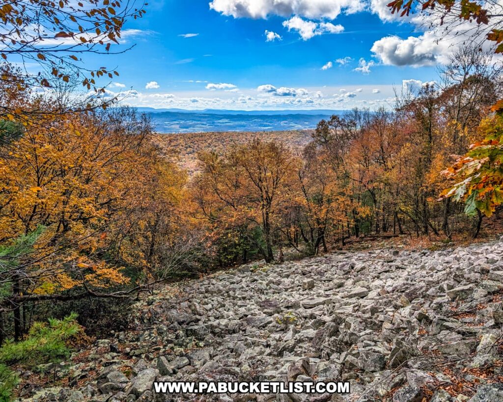 Rocky overlook along the Pump Station Trail near Harry’s Valley Vista in Rothrock State Forest, showcasing colorful autumn trees and layered mountain ridges stretching into the distance under a bright blue sky with scattered clouds.