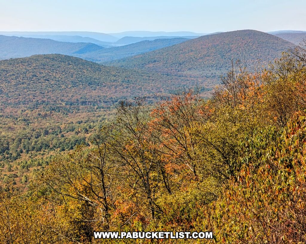 Magnified autumn view from Harry’s Valley Vista in Rothrock State Forest, showing layers of forested ridges and rounded mountains fading into the hazy blue distance under a clear sky.