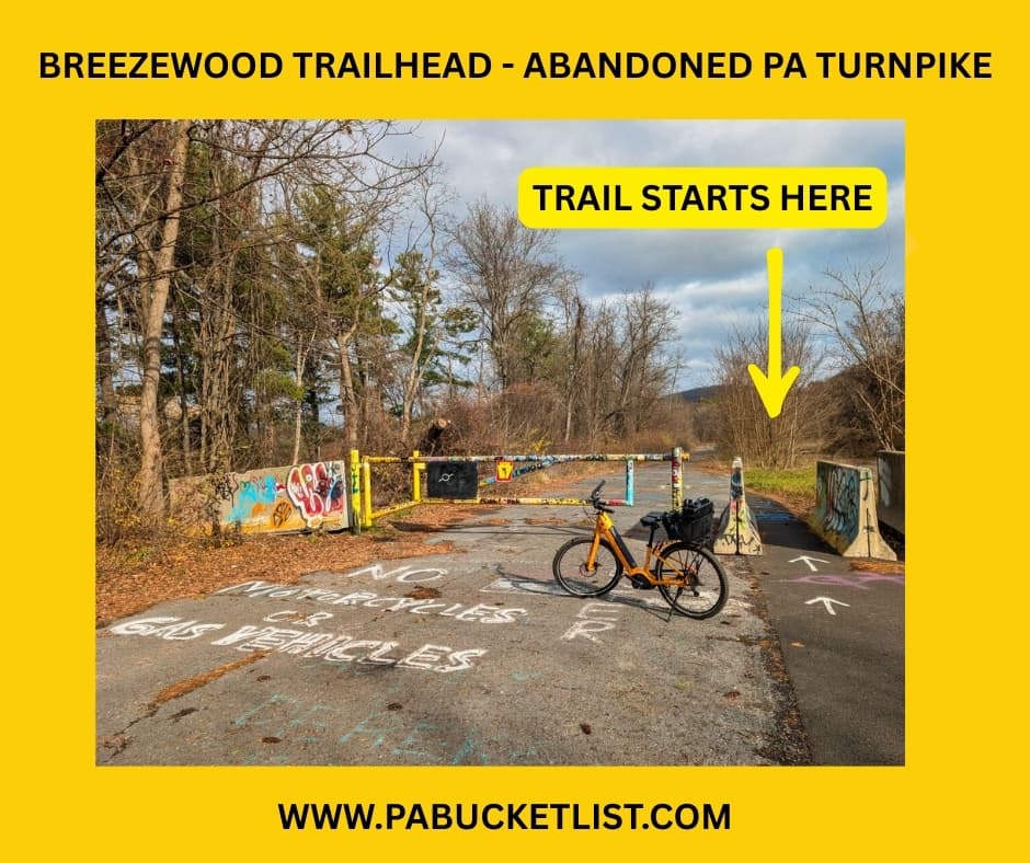 Yellow-highlighted photo showing the Breezewood Trailhead entrance to the Abandoned PA Turnpike, with an orange bicycle parked beside a graffiti-covered barrier and an arrow indicating where the 8.5-mile former Turnpike trail begins in Bedford and Fulton counties.