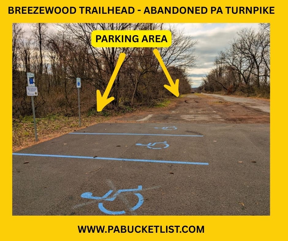Photo of the Breezewood Trailhead showing newly painted accessible parking spaces beside the cracked pavement of the Abandoned PA Turnpike, with arrows indicating the adjacent parking area at the western end of the 8.5-mile former Turnpike trail in Bedford and Fulton counties.