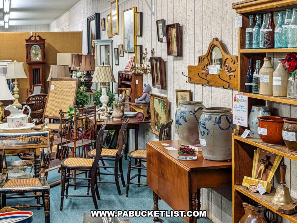 Aisle filled with antique furniture, stoneware crocks, cane-seated chairs, framed artwork, table lamps, bottles, and decorative home goods at Collector’s Choice Antiques Gallery in New Oxford, Pennsylvania.