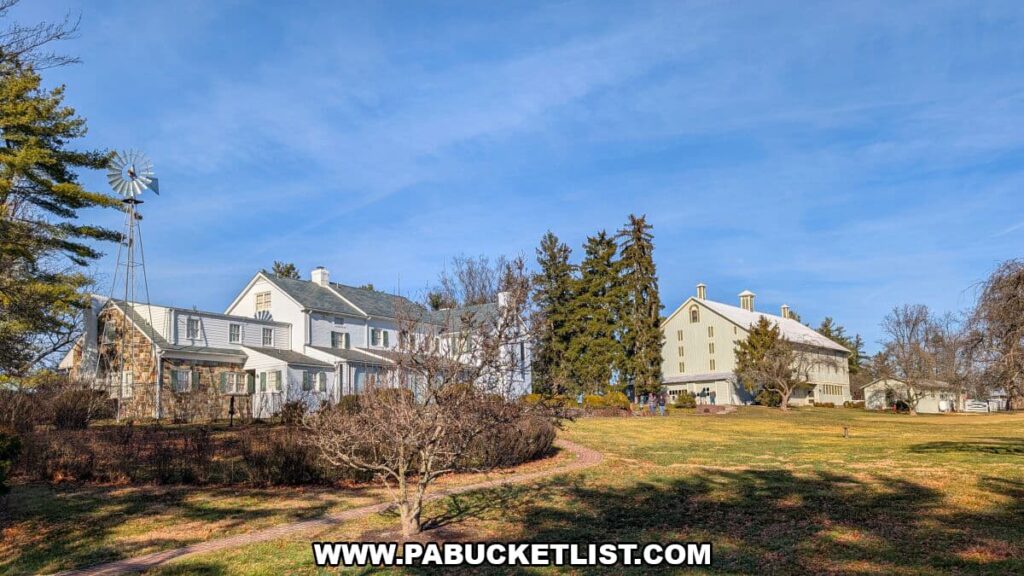 Wide view of the Eisenhower National Historic Site showing the white farmhouse and large barn set amid rolling fields, dormant winter landscaping, tall evergreens, and a towering metal windmill under a bright blue Pennsylvania sky.