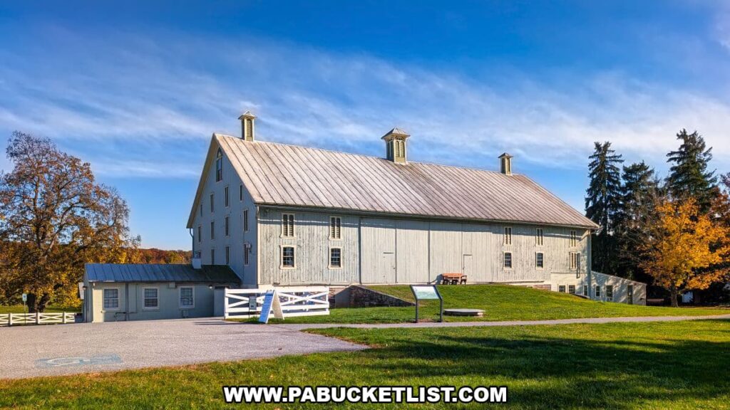 Large white barn at the Eisenhower National Historic Site set against a bright blue sky, with cupolas on the roof, a white fence, informational sign, and surrounding fields and autumn trees in Gettysburg.