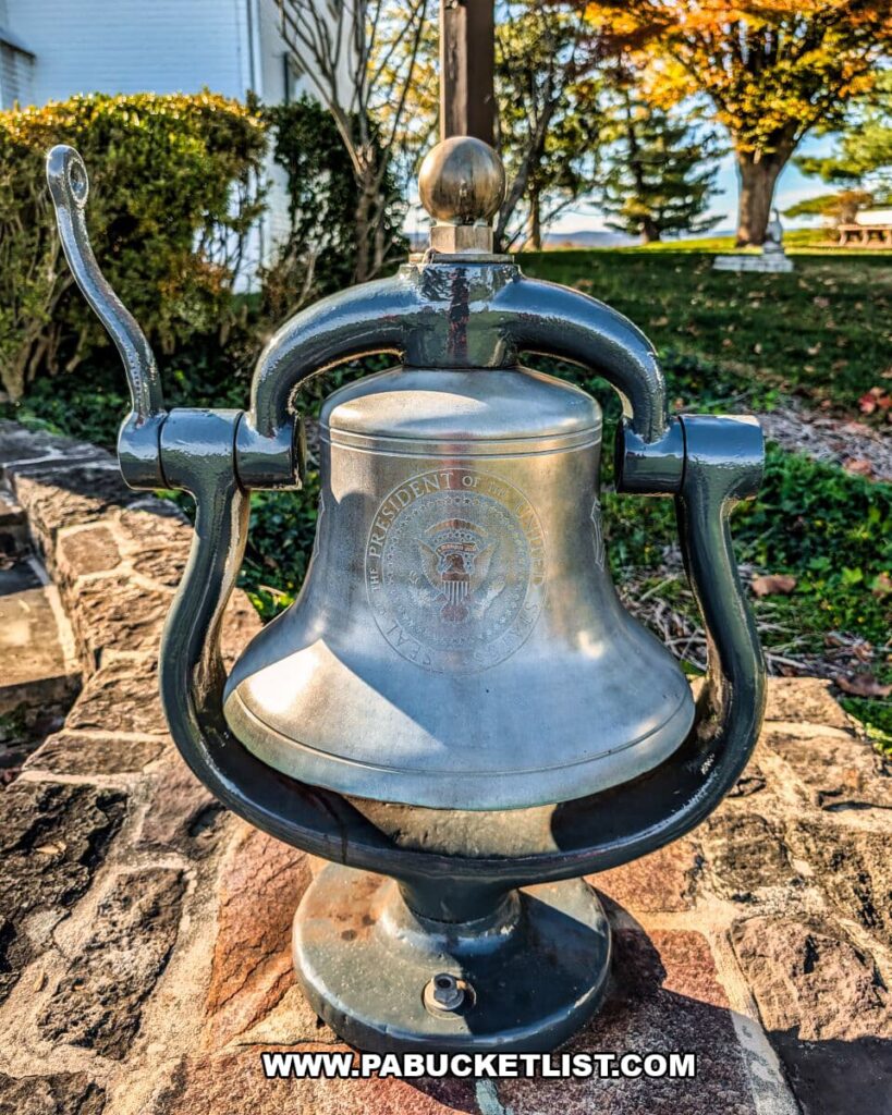 Outdoor dinner bell bearing the Presidential Seal at the Eisenhower National Historic Site, mounted on a stone wall near the farmhouse with autumn trees and lawn in the background.