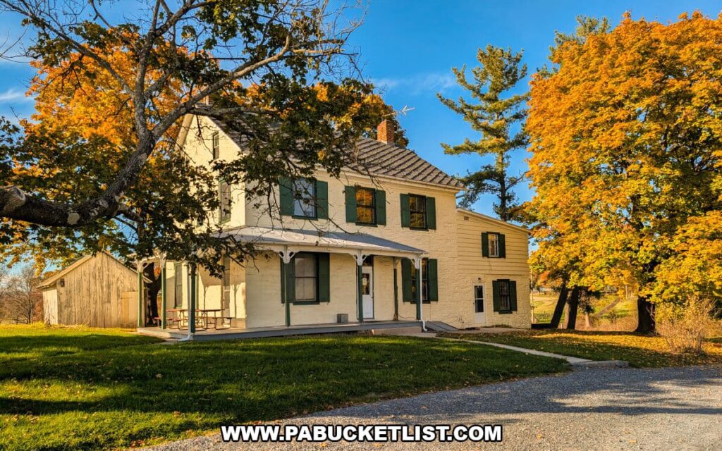Herdsman’s house at the Eisenhower National Historic Site, a cream-colored two-story home with green shutters and a porch, surrounded by golden autumn trees and a nearby wooden shed under a blue sky.