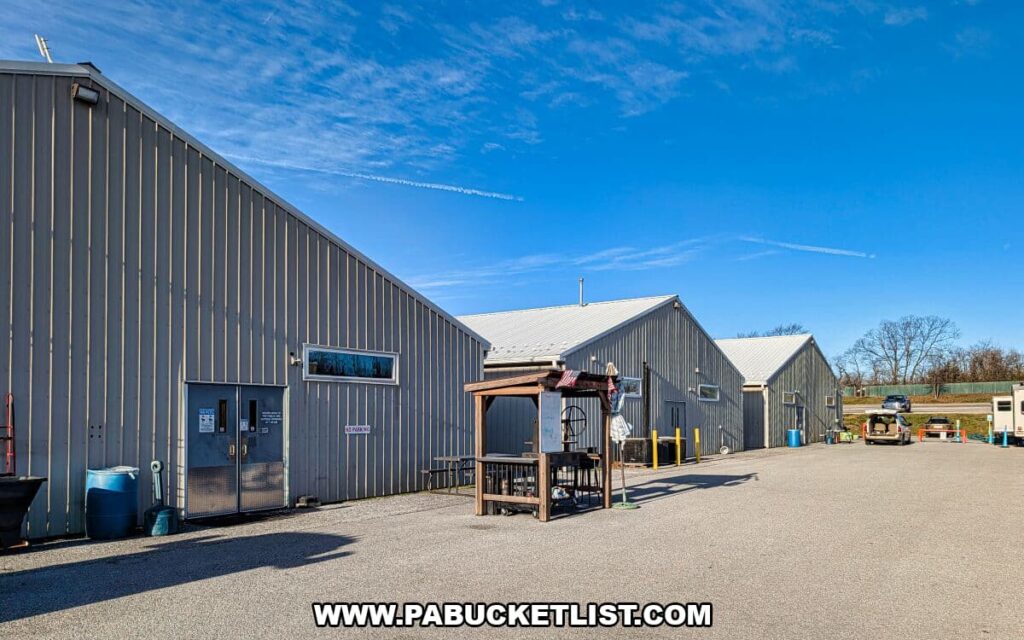 Exterior view of the large gray warehouse-style buildings at Morning Sun Marketplace in York County, PA, with a small outdoor vendor stand and parked vehicles under a bright blue sky.