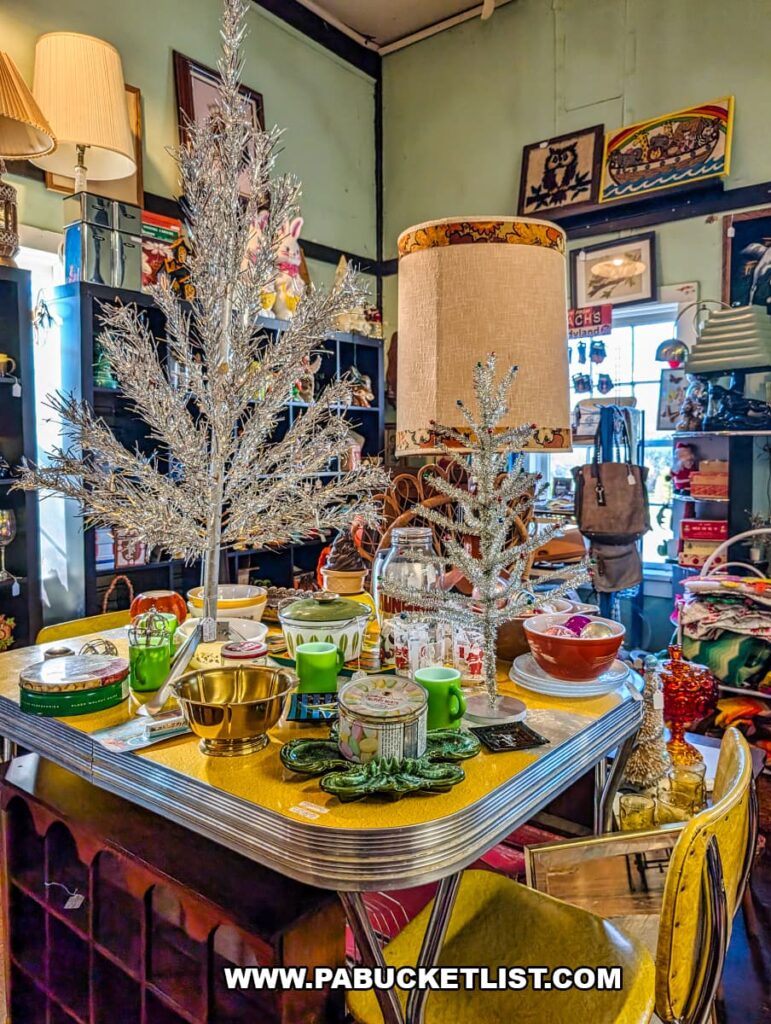 Mid-century modern table display inside American Daydream Antiques in York County, Pennsylvania, featuring vintage aluminum Christmas trees, colorful glassware, retro lamps, holiday decor, and eclectic collectibles arranged within a multi-vendor antique shop
