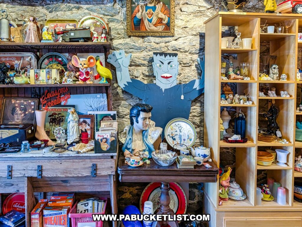 Eclectic interior display at American Daydream Antiques in York County, Pennsylvania, featuring vintage glassware, religious art, pop culture figurines, advertising tins, retro toys, framed photos, and home decor arranged against a stone wall in a multi-vendor antique store