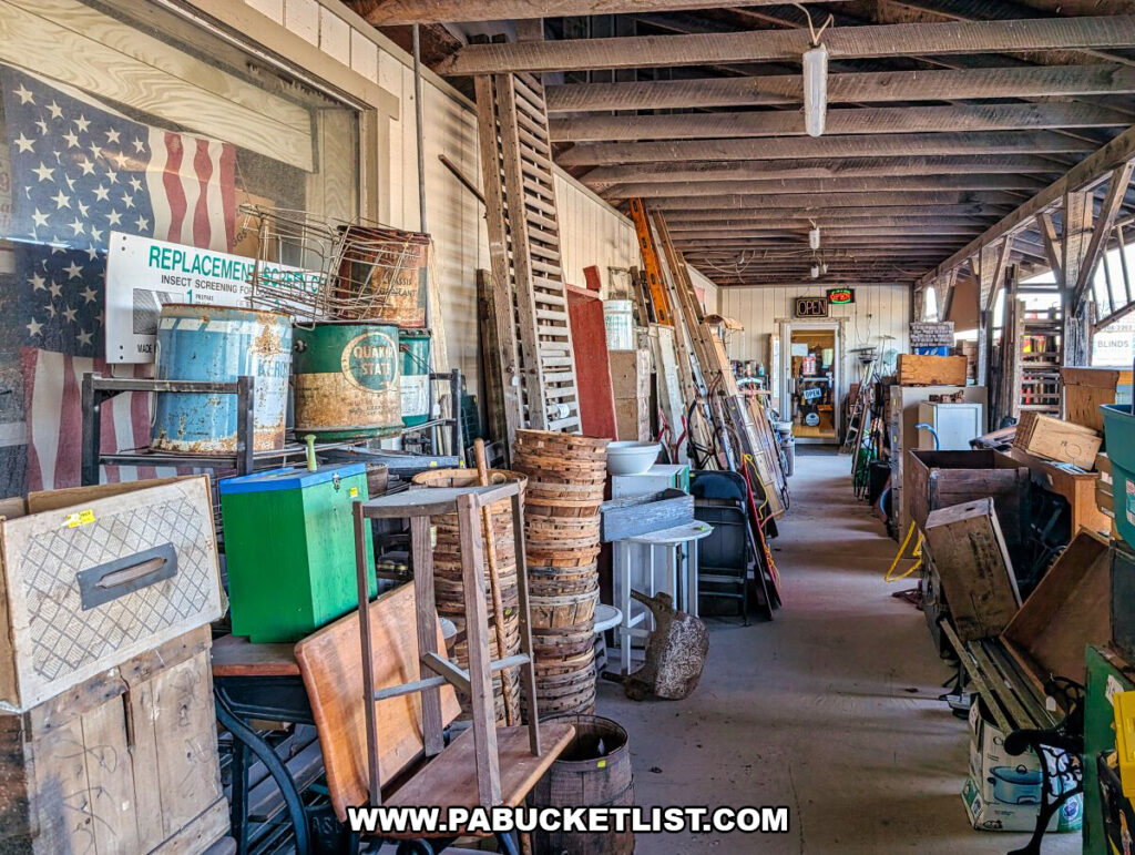 A long covered interior walkway at Black Shutter Antiques in New Oxford, Pennsylvania, filled with vintage cabinets, wooden crates, baskets, doors, signs, tools, and architectural salvage displayed along both sides of the multi-vendor antique store