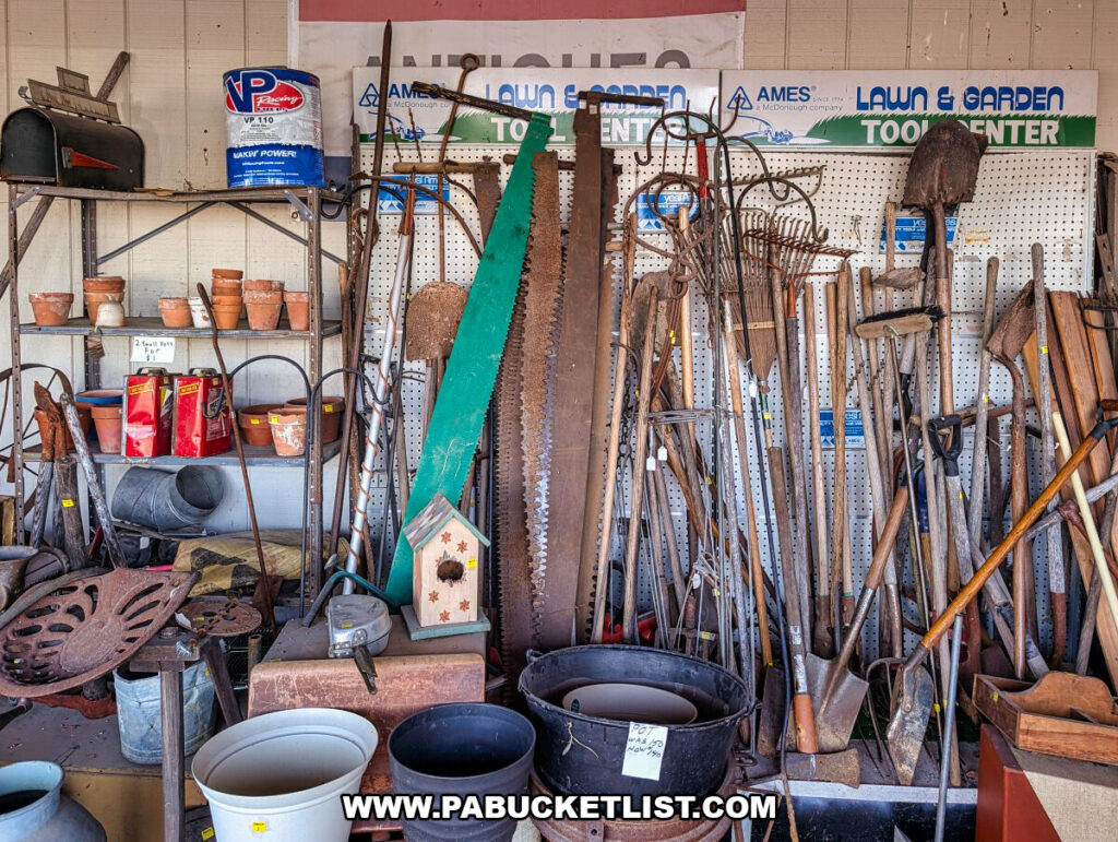 A wall display at Black Shutter Antiques in New Oxford, Pennsylvania, featuring antique hand tools, saws, shovels, rakes, garden implements, and rustic hardware arranged against pegboard inside the multi-vendor antique store