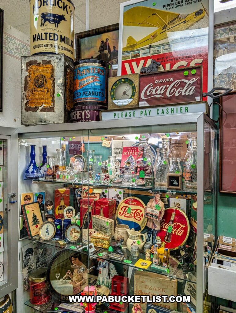 Glass display case at Crossroads Antique Mall in Hershey, Pennsylvania, filled with vintage Coca-Cola and Pepsi memorabilia, antique bottles, tins, advertising signs, clocks, and nostalgic packaging from early 20th-century brands.