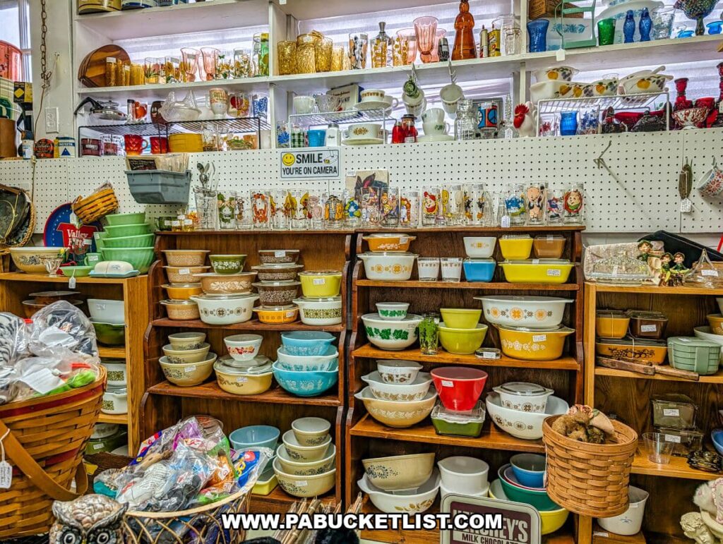 Vendor display at Crossroads Antique Mall in Hershey, Pennsylvania, showcasing shelves filled with colorful vintage Pyrex casserole dishes, mixing bowls, patterned glassware, and mid-century kitchen collectibles arranged in a cozy barn interior.