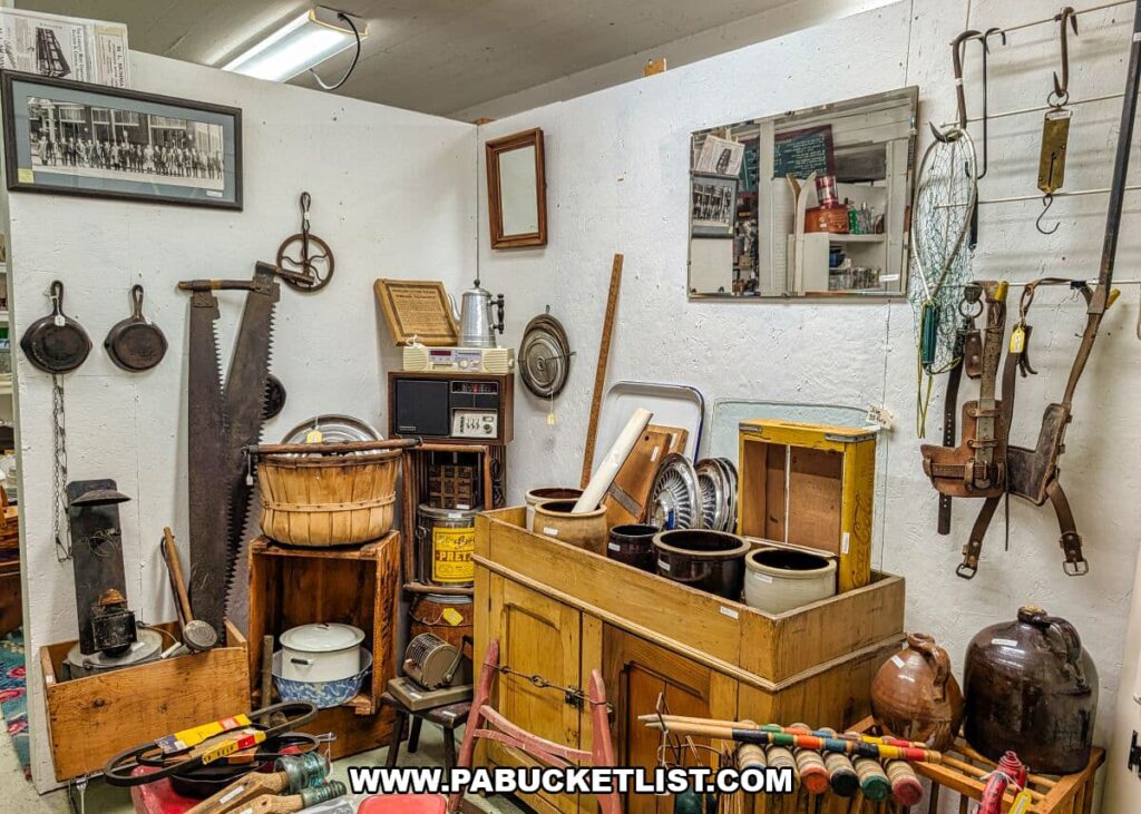 Rustic vendor booth at Crossroads Antique Mall in Hershey, Pennsylvania, featuring antique hand tools, saws, wooden crates, crocks, jugs, wash tubs, farm equipment, and early household items displayed against white barn walls.