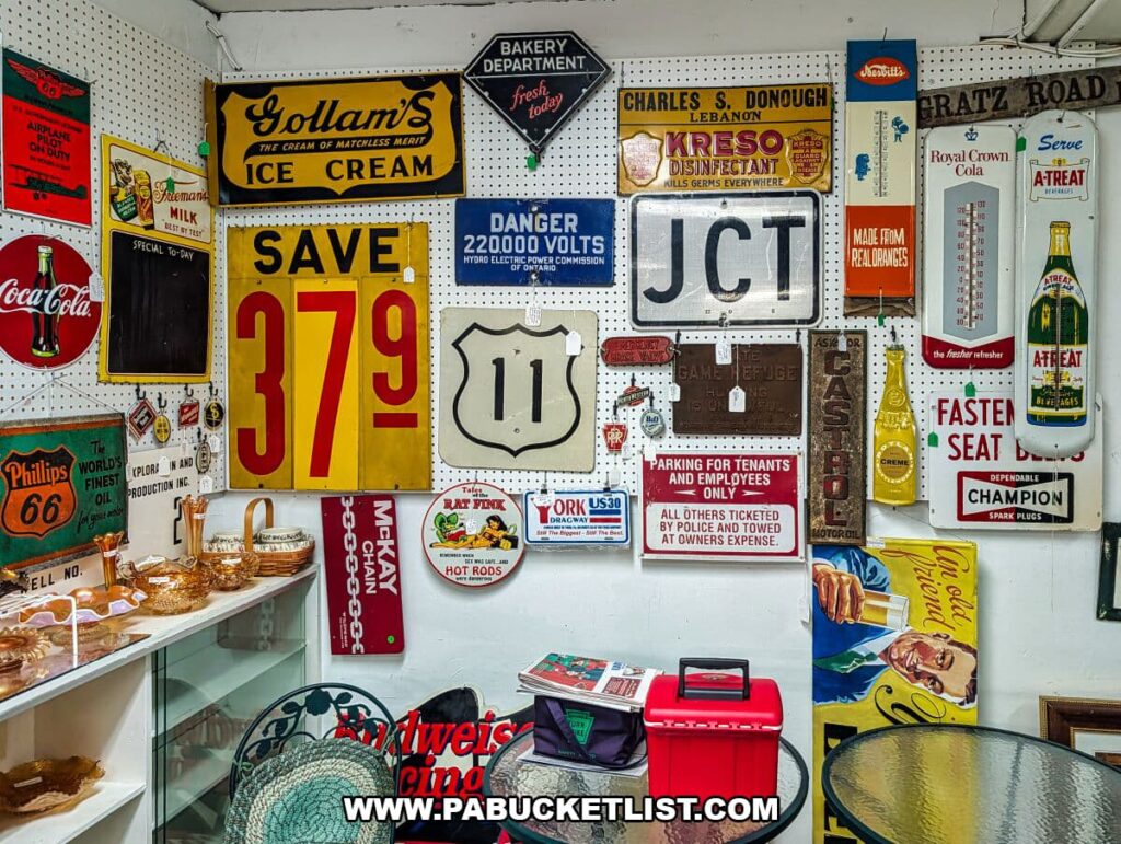 Wall display at Crossroads Antique Mall in Hershey, Pennsylvania, covered with colorful vintage advertising and road signs including ice cream, Coca-Cola, motor oil, gas, safety warnings, and Route 11 signage arranged on pegboard inside the historic barn.