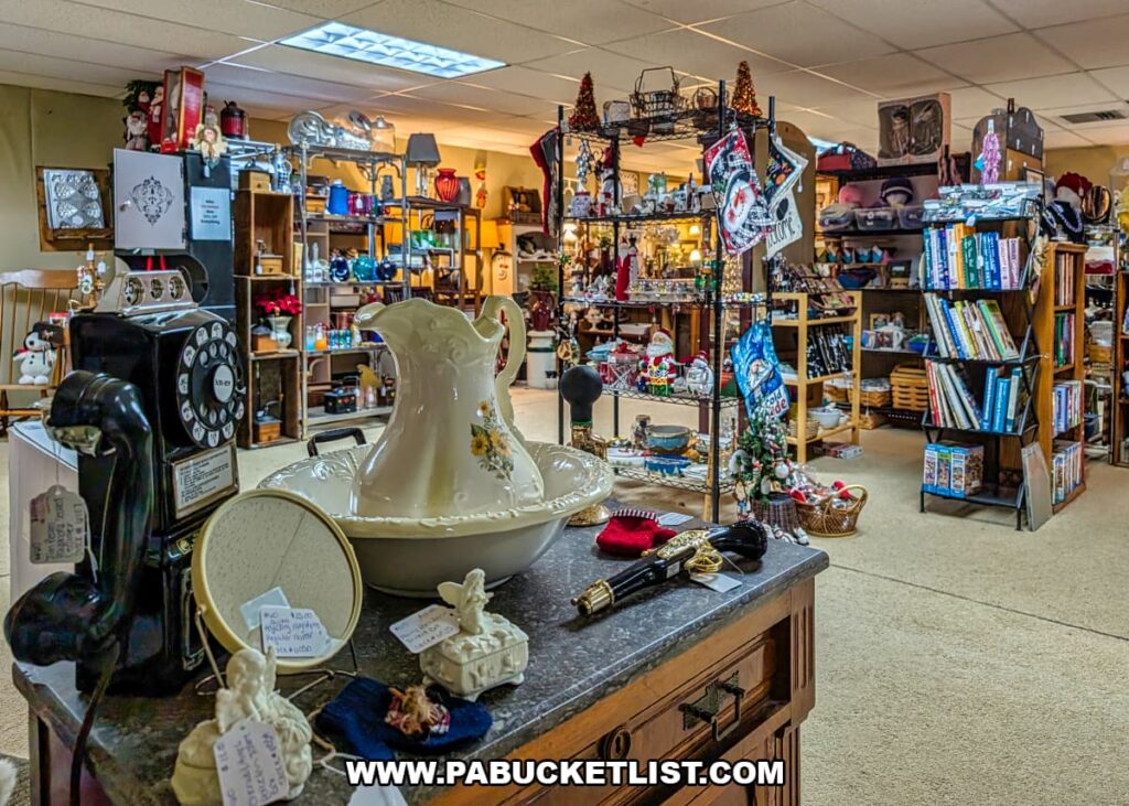 Interior view of a vendor booth at Dover Antique Mall in York County, Pennsylvania, featuring a tabletop display of vintage ceramics, a rotary telephone, figurines, and small collectibles, with shelves of books, home décor, and antiques from multiple vendors filling the background.