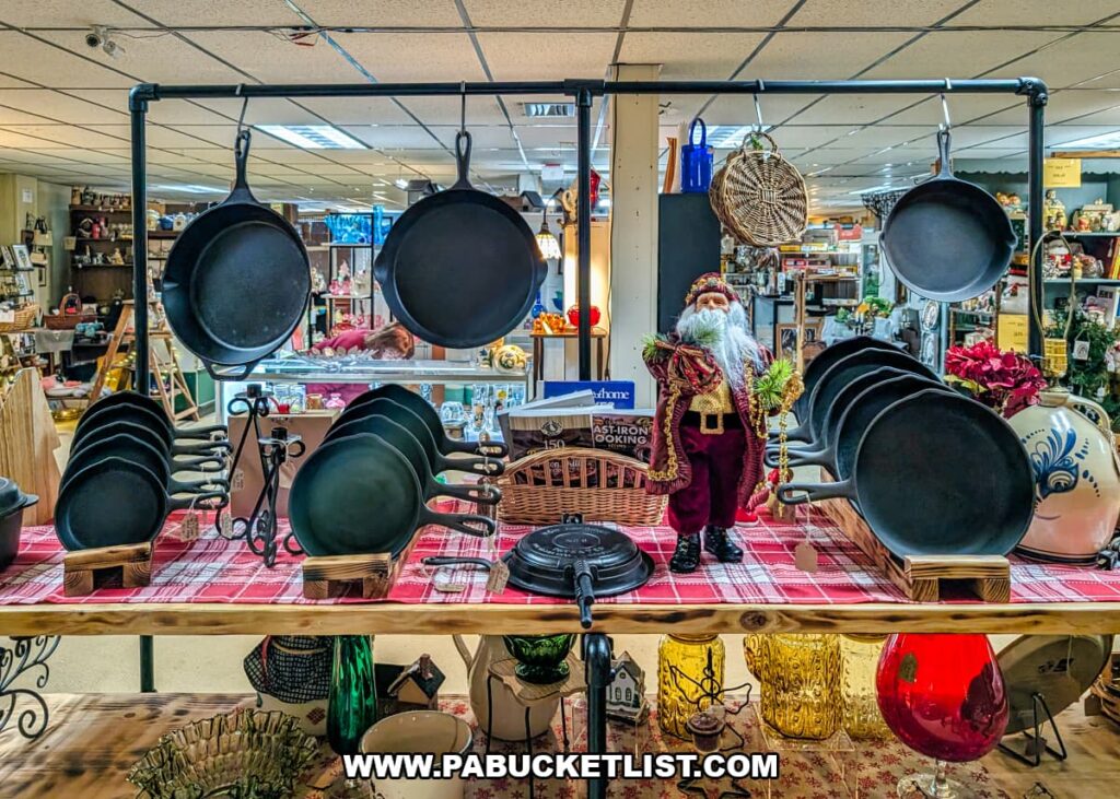 Display of vintage cast iron skillets and cookware at Dover Antique Mall in York County, Pennsylvania, with multiple pans hanging and stacked on a wooden table alongside rustic kitchen items and decorative accents inside the multi-vendor antique mall.