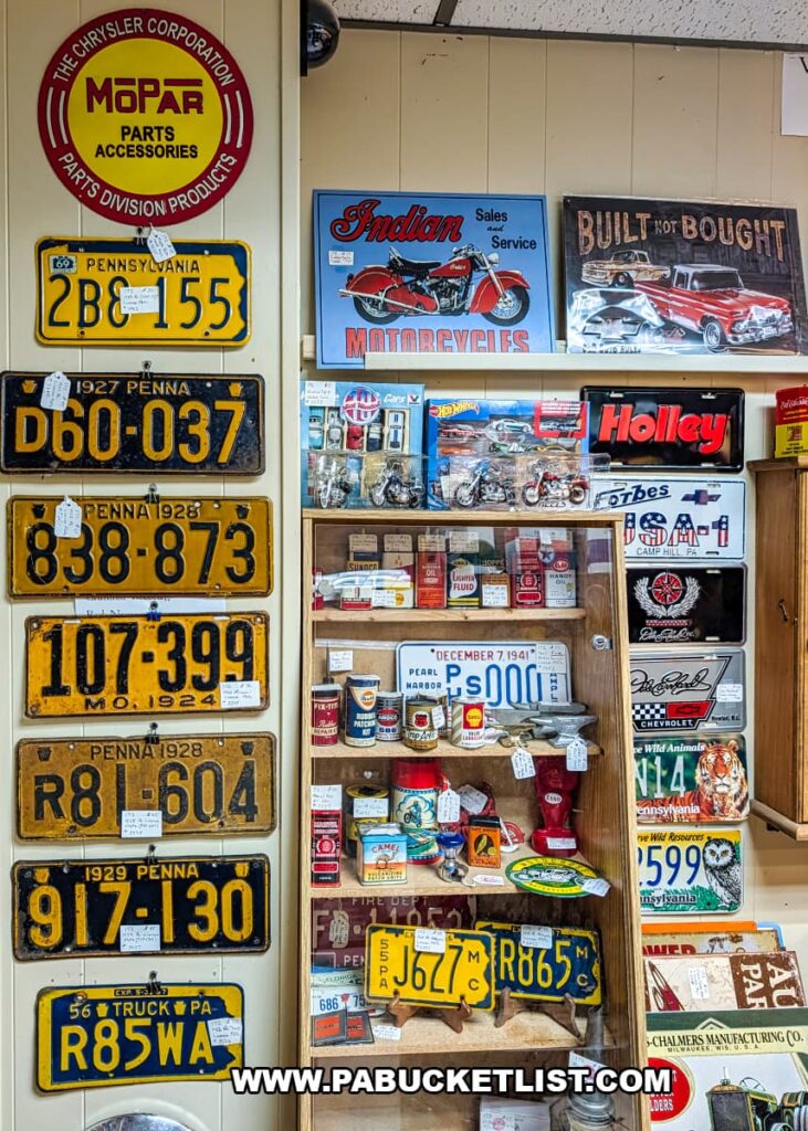 Wall display inside Dover Antique Mall in York County, Pennsylvania, featuring a vertical row of vintage Pennsylvania license plates alongside automotive signs, motorcycle memorabilia, old oil cans, and car-related collectibles arranged in a glass cabinet.
