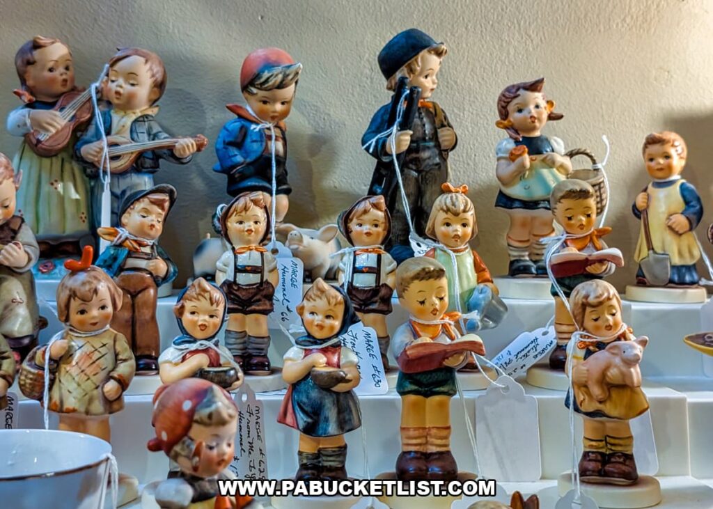 Collection of vintage Hummel-style figurines displayed on tiered shelves at Grey Beards Antiques in York County, Pennsylvania, featuring hand-painted child figures with musical instruments, books, and baskets inside a vendor booth at the multi-vendor antique mall in Jacobus.
