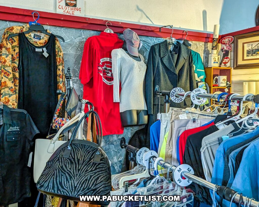 Vintage clothing and accessories displayed on racks and mannequins at Grey Beards Antiques in York County, Pennsylvania, featuring jackets, graphic T-shirts, handbags, and assorted apparel inside a vendor booth at the multi-vendor antique mall in Jacobus.