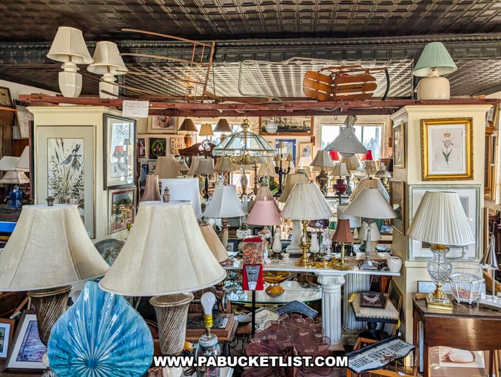 Large selection of vintage table and floor lamps displayed throughout a vendor space at Grey Beards Antiques in York County, Pennsylvania, featuring assorted lamp bases, shades, framed artwork, and architectural decor inside the multi-vendor antique mall in Jacobus.