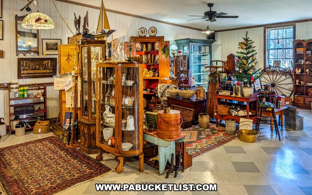 Spacious vendor booth displaying antique furniture, glass display cabinets, pottery, wall art, baskets, rugs, and rustic home decor arranged like a vintage room setting inside Shrewsbury Antique Center in York County, Pennsylvania.