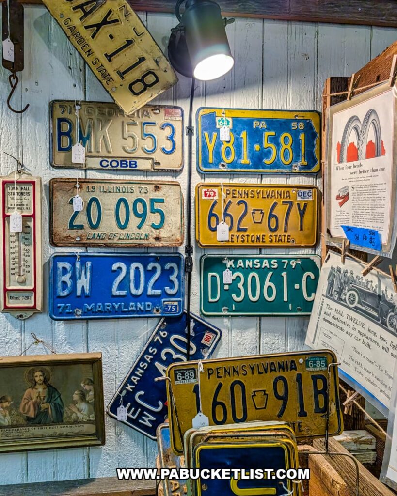 Wall display of vintage metal license plates from Pennsylvania and other states, along with old signs and framed ephemera, inside a vendor booth at Shrewsbury Antique Center in York County, Pennsylvania.
