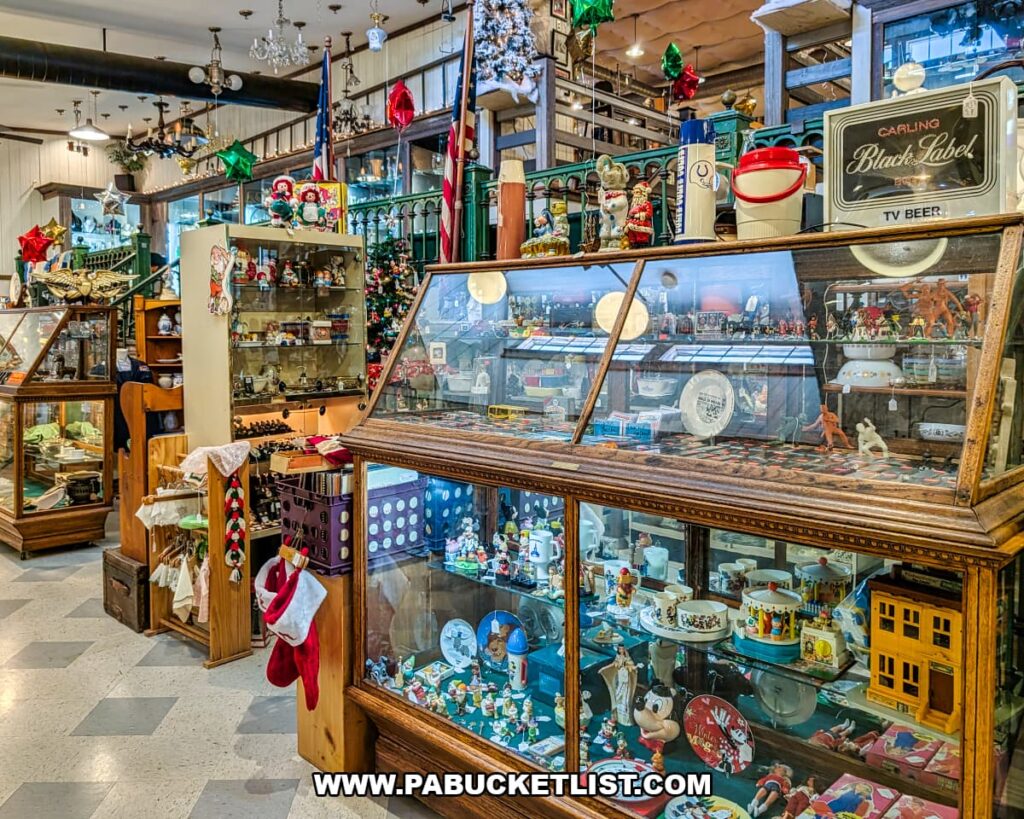 Interior aisle view showing glass display cases filled with vintage toys, figurines, glassware, and collectibles, with holiday decorations and multiple vendor booths inside Shrewsbury Antique Center in York County, Pennsylvania.