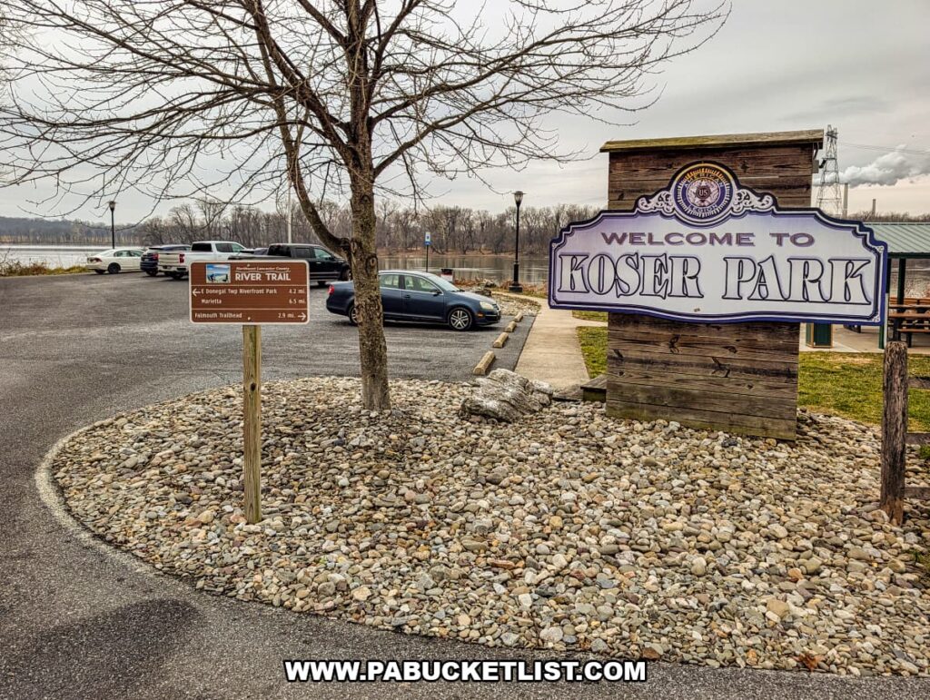Entrance sign for Koser Park and the Northwest Lancaster County River Trail trailhead, with parking area, trail signage, and the Susquehanna River visible nearby in Lancaster County, Pennsylvania.