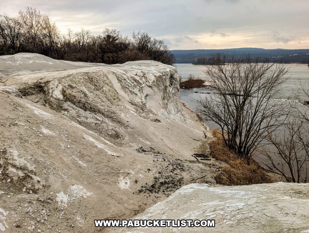 Chalky quarry cliff edge at the White Cliffs of Conoy sloping down toward the Susquehanna River, with leafless trees and distant hills visible along the riverbank in Lancaster County, Pennsylvania.