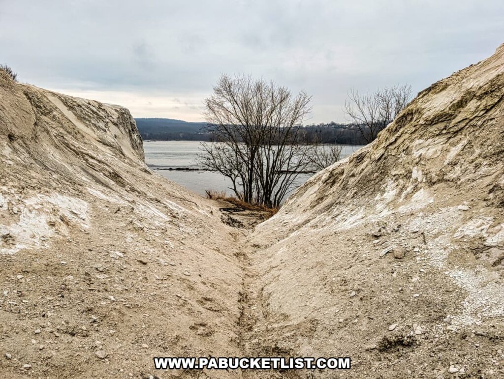 Narrow eroded ravine between chalky quarry mounds at the White Cliffs of Conoy, leading toward views of the Susquehanna River and distant hills in Lancaster County, Pennsylvania.
