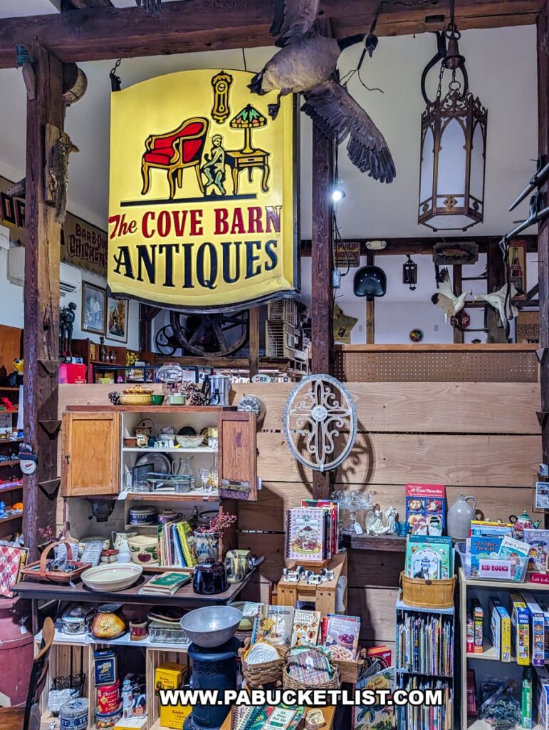 Interior of Cove Barn Antiques in Duncannon, Pennsylvania, displaying shelves of vintage kitchenware, books, collectibles, and rustic decor beneath a hanging antique sign inside a repurposed barn interior