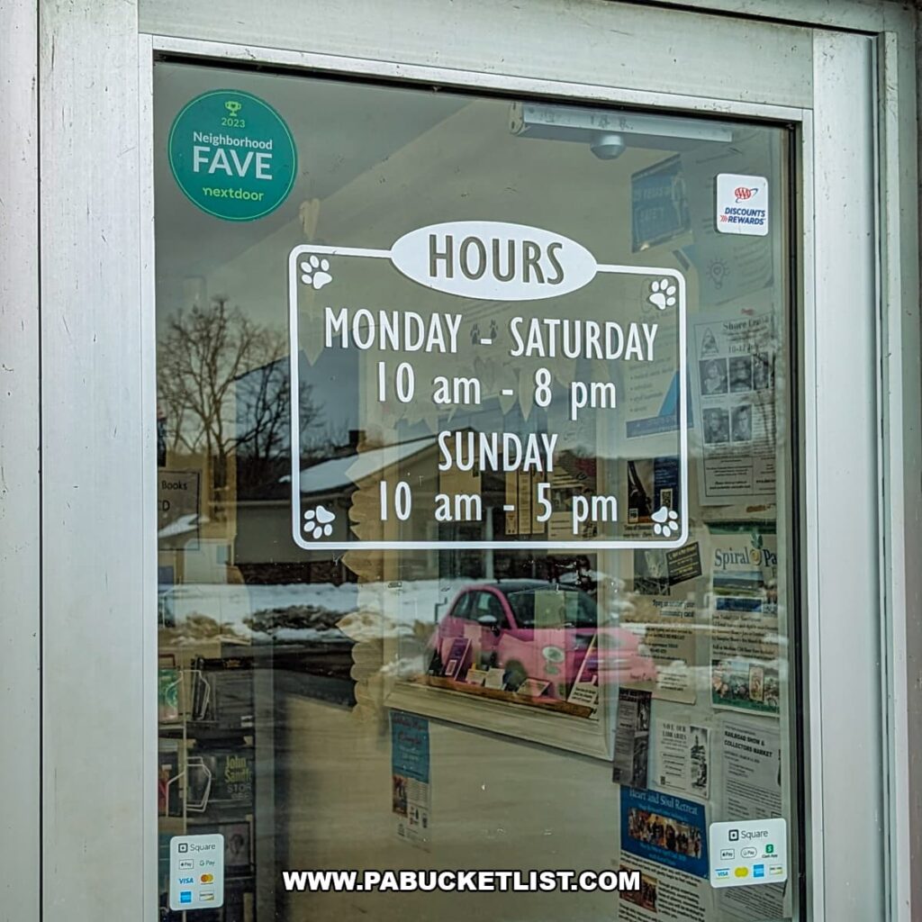 Front door window at Cupboard Maker Books in Cumberland County, Pennsylvania, displaying store hours for Monday through Sunday with paw print accents, reflecting the welcoming, cat-themed charm of the community-focused bookstore.