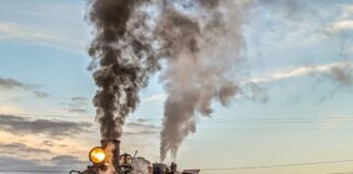 Steam locomotive No. 16 of the East Broad Top Railroad in Huntingdon County, Pennsylvania, billows smoke and steam as it pulls vintage passenger cars along the tracks at sunset.