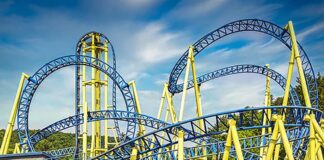 Group of kids watch the Impulse roller coaster at Knoebels Amusement Park in Columbia County, Pennsylvania, as the blue and yellow track twists and loops overhead on a sunny day.