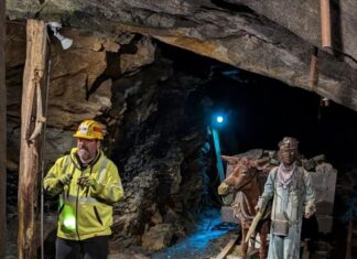 A Complete Guide to PA’s Best Underground Coal Mine Tours Tour guide in a hard hat leads visitors through the Lackawanna Coal Mine Tour in Scranton, Pennsylvania, passing historic mine rails and a display featuring a mule and miner statue deep inside the underground tunnel.