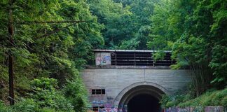 Entrance to the abandoned Rays Hill Tunnel along the Pennsylvania Turnpike in Bedford County, Pennsylvania, with colorful graffiti and chalk drawings covering the roadway leading into the dark tunnel beneath a wooded hillside.